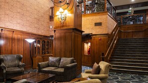 Un vestíbulo con una imponente escalera, sofás de cuero y un mostrador de recepción de madera.
