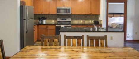 A modern kitchen with wooden cabinets, stainless steel appliances, and a dining area with a wooden table and chairs.
