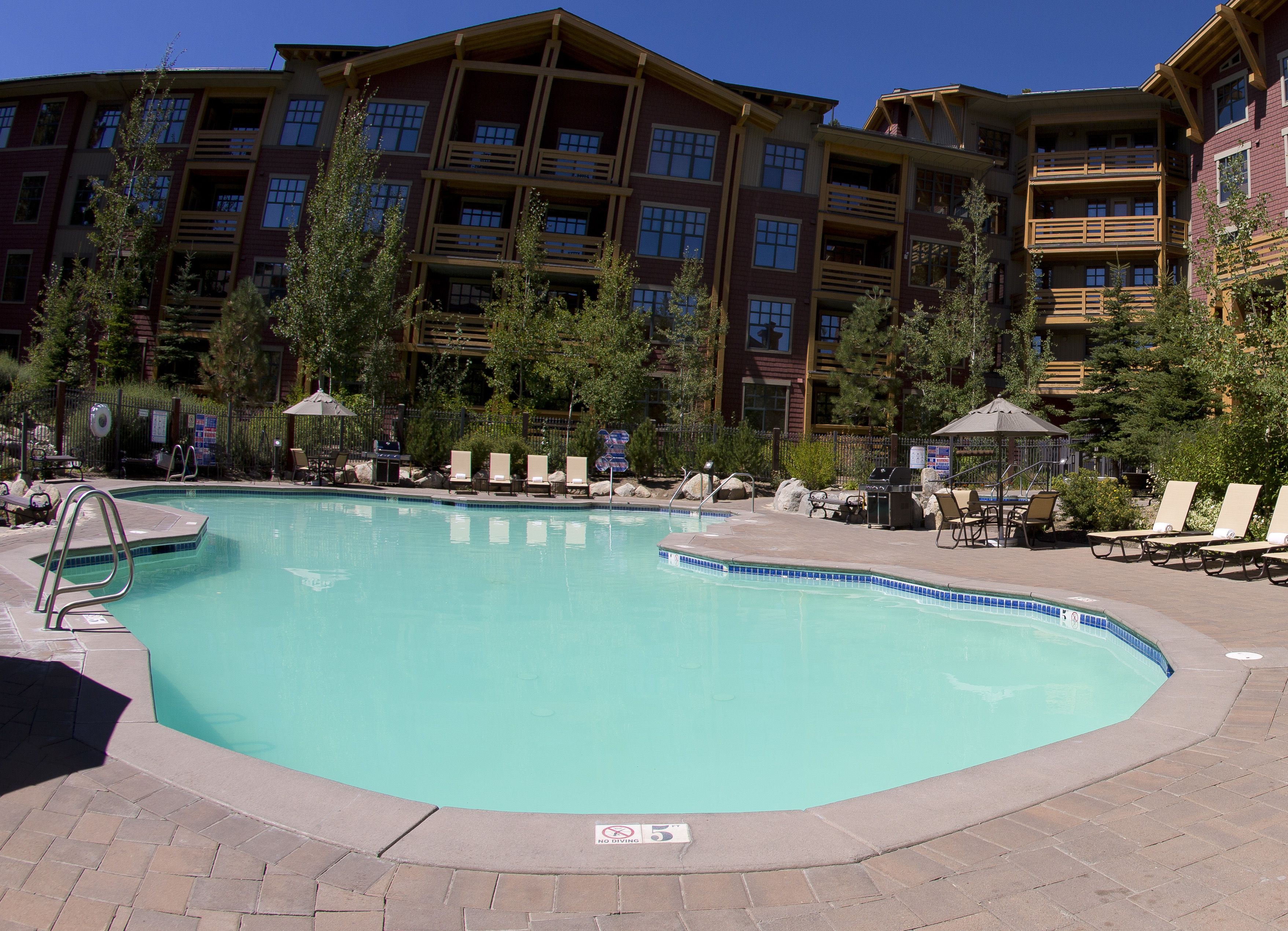 A swimming pool with lounge chairs and umbrellas, surrounded by a building with multiple balconies.