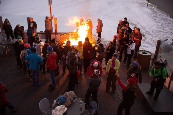 A group of people gathered around a fire pit on a wooden deck.