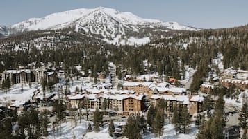 A snow-covered mountain resort with multiple buildings, including a lodge and a hotel, surrounded by dense forests.