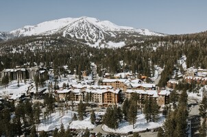 A snow-covered mountain resort with multiple buildings, including a lodge and a hotel, surrounded by dense forests.