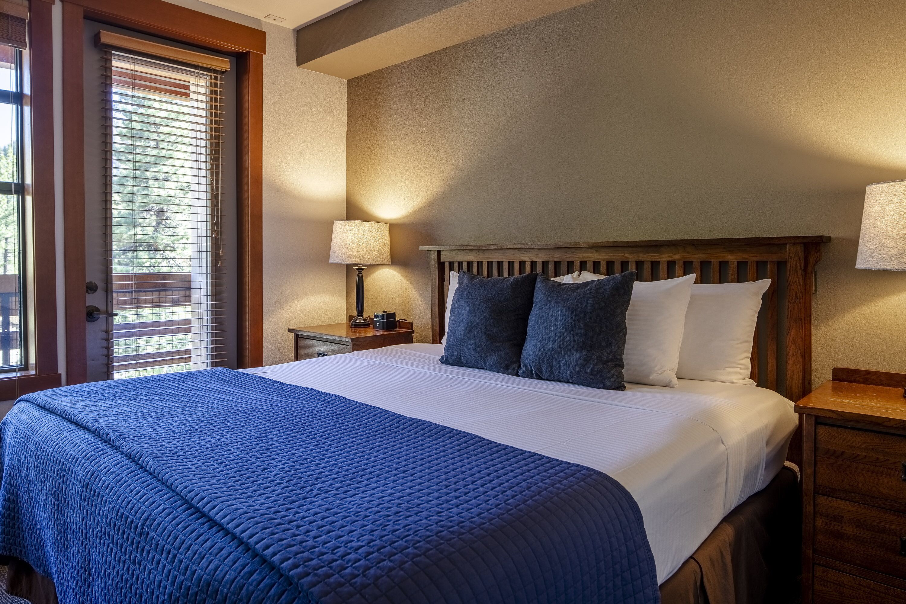 A neatly made bed with a blue quilt, a wooden headboard, and a nightstand with a lamp.
