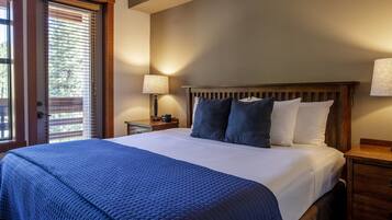 A neatly made bed with a blue quilt, a wooden headboard, and a nightstand with a lamp.