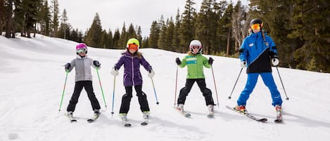Four skiers on a snowy slope with trees in the background.
