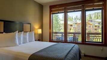 Camera d'albergo con un letto grande, una testiera, una finestra che si affaccia su edifici e alberi, e una ventola a soffitto.