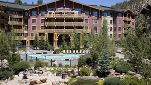 Un hotel de varios pisos con piscina, zona de estar exterior y montañas al fondo.