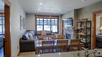 A modern kitchen with granite countertops, a dining area with wooden chairs, a stone fireplace, and a large window with blinds.