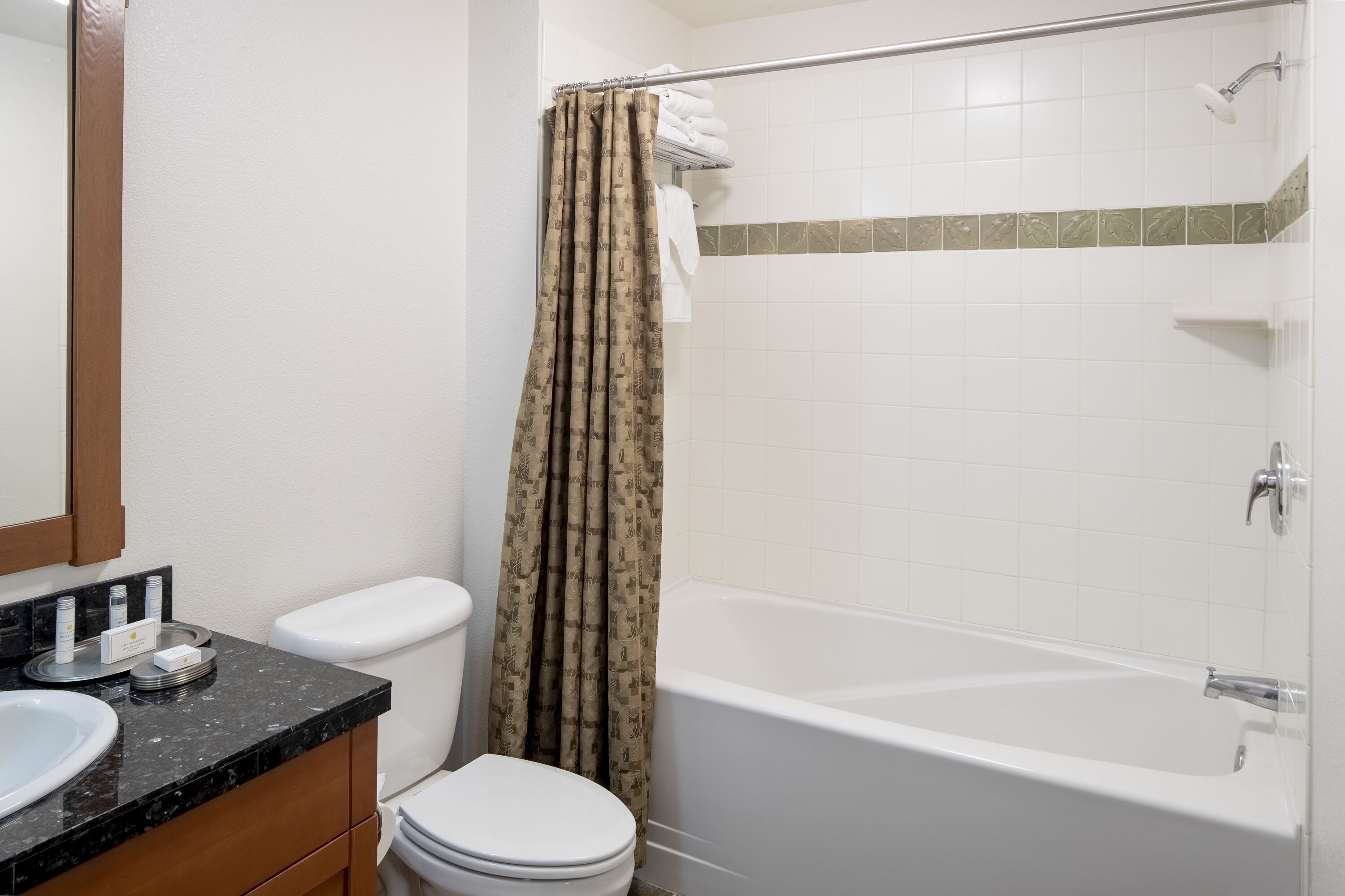 A bathroom with a white toilet, a sink with a black countertop, a shower with a beige curtain, and a bathtub.