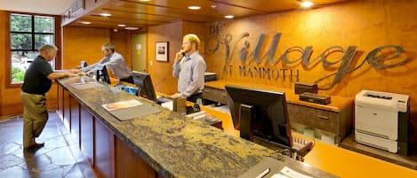 A reception desk with a stone floor, wooden paneling, and a sign reading "The Village at Mammoth."