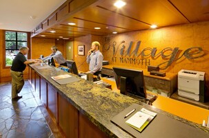 Un mostrador de recepción con suelo de piedra, paneles de madera y un cartel que dice "The Village at Mammoth".