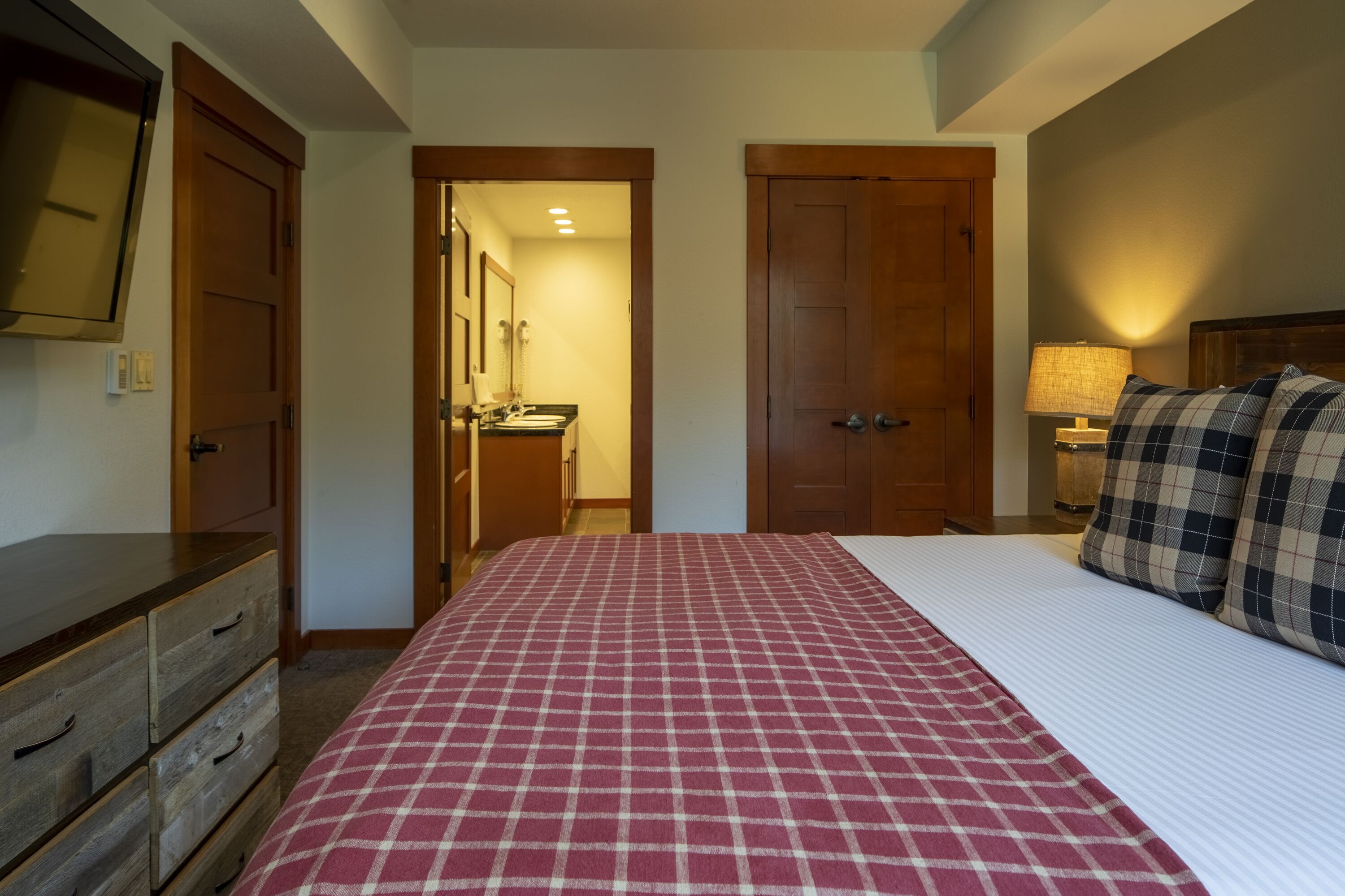 A hotel room with a bed, a dresser, a mirror, and a door leading to a bathroom.