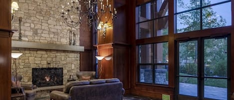 A spacious living room with a stone fireplace, leather sofas, and large windows offering a view of the outdoors.
