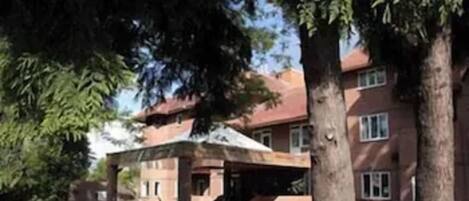 Un edificio de varios pisos con estacionamiento techado, rodeado de árboles y follaje.