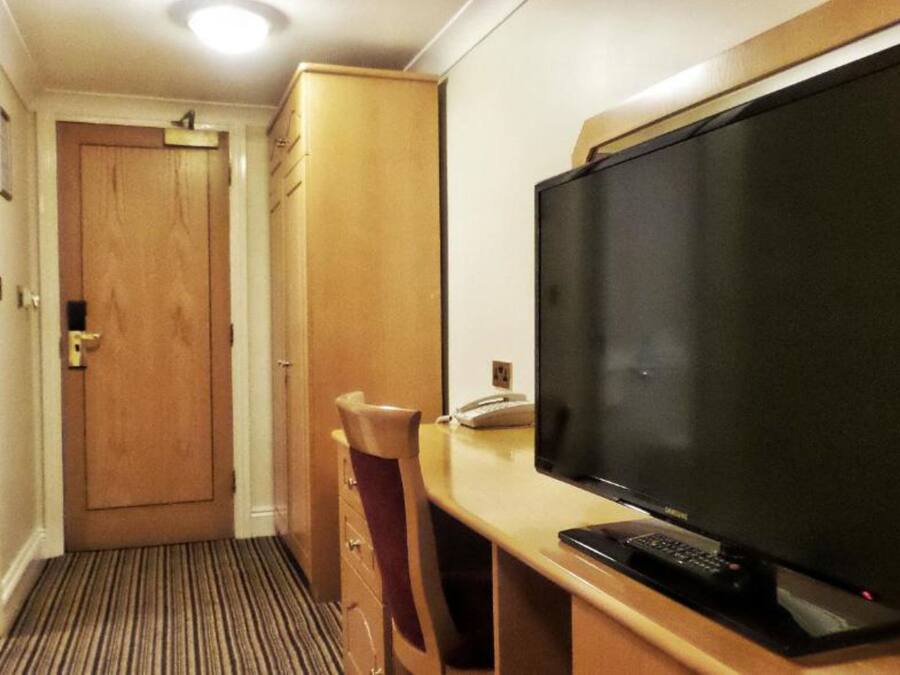 Una habitación de hotel con una puerta de madera, un escritorio con televisor y un teléfono.