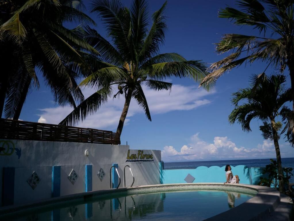 A pool area with palm trees, a clear sky, and a view of the ocean.