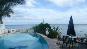Une piscine avec l’inscription « Las Flores », entourée de chaises et d’un parasol, et offrant une vue sur la mer.