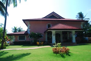 A two-story house with a red-tiled roof, a covered porch, and a well-maintained lawn. - Las Flores Country & Beachside Hotel (Catmon)