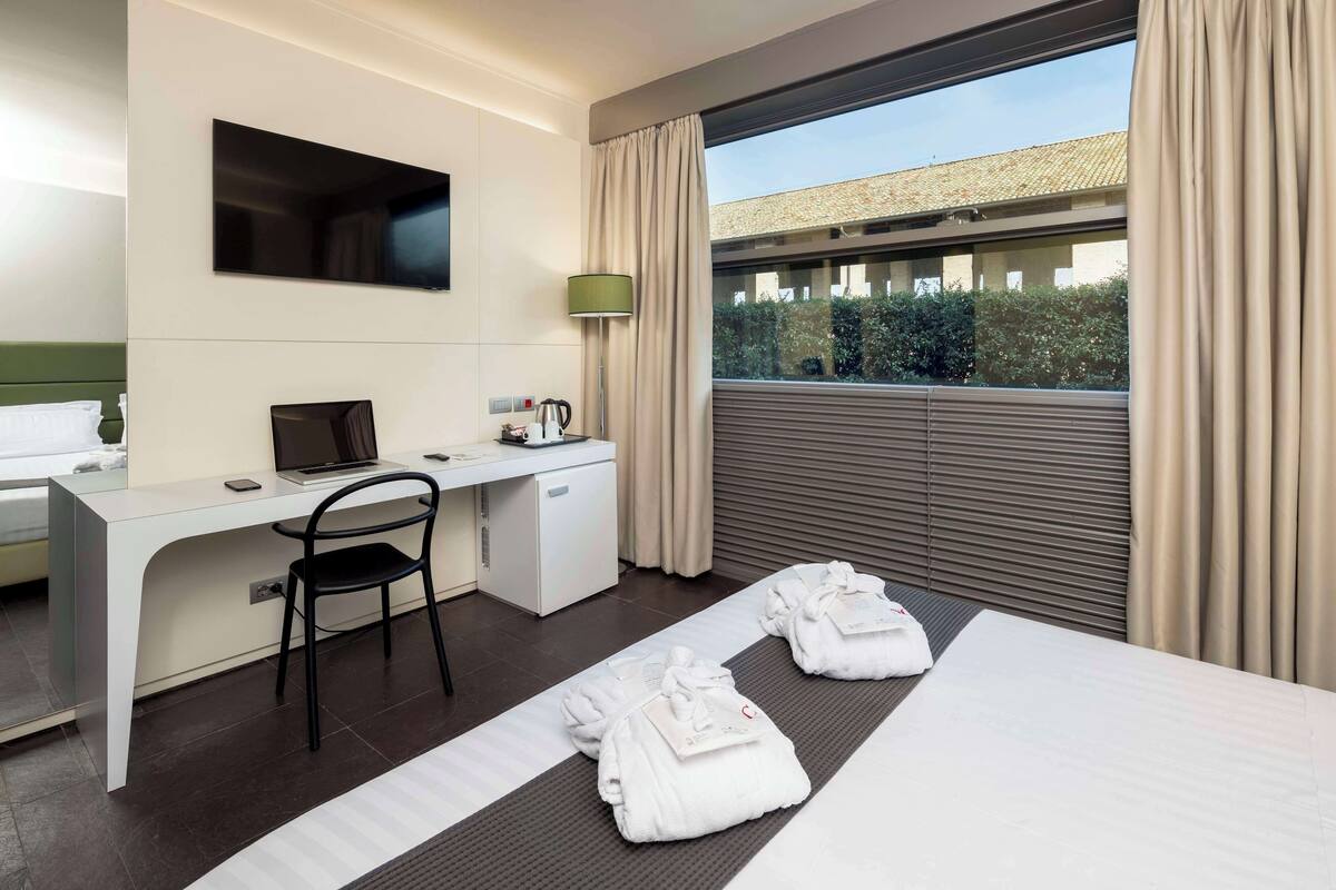 A hotel room with a bed, a desk, a chair, a TV, and a window with curtains.