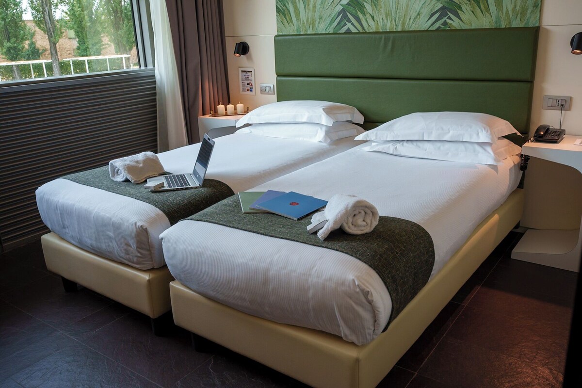 A hotel room with two beds, a laptop on one bed, a book on the other, and a phone on the nightstand.