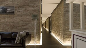 A corridor with a brick wall, a framed picture, a modern light fixture, and a leather sofa. - Best Western Hotel Green City (Parma)