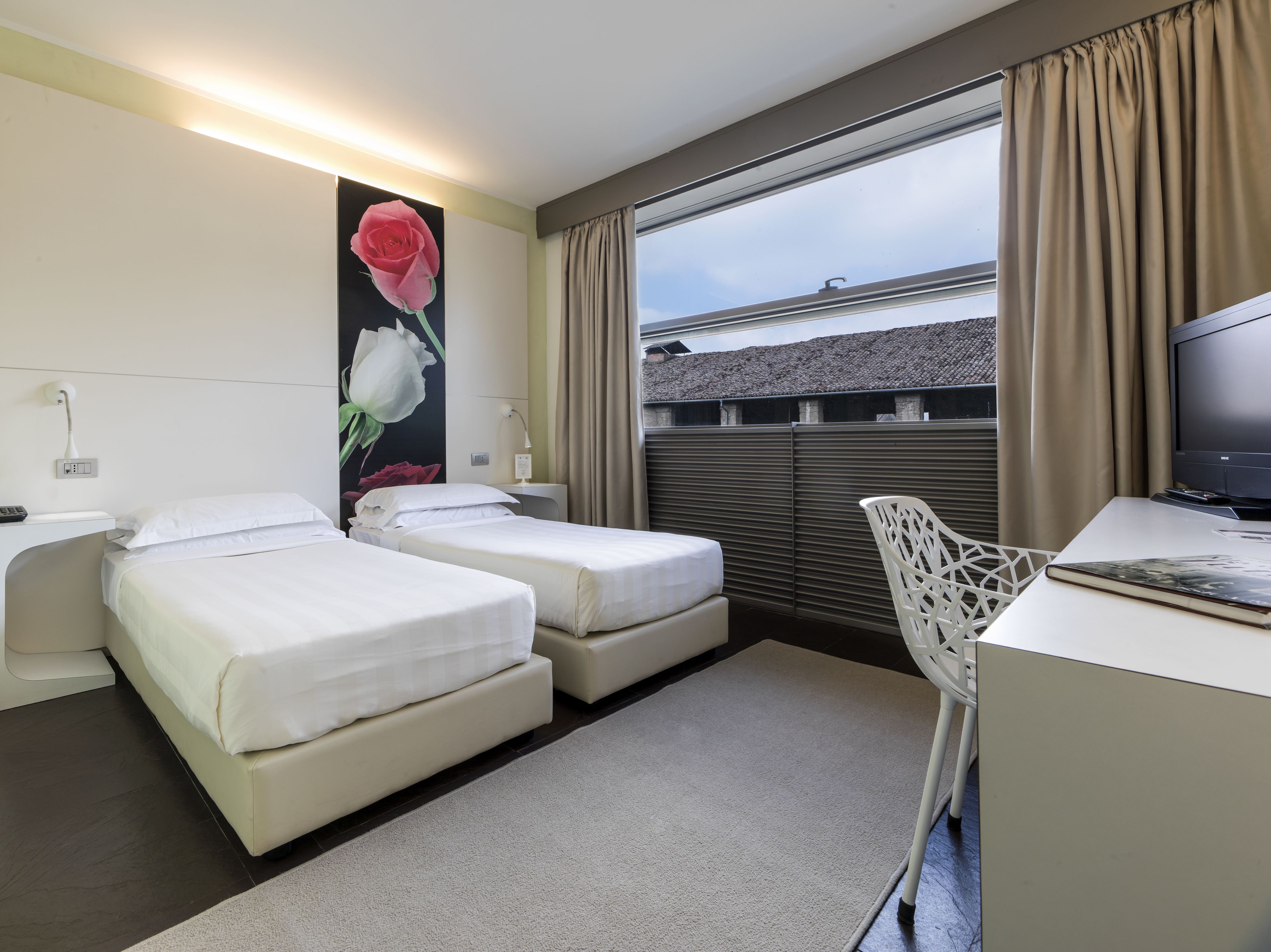 Habitación de hotel con dos camas, un escritorio, una silla, un televisor y un ventanal con cortinas.