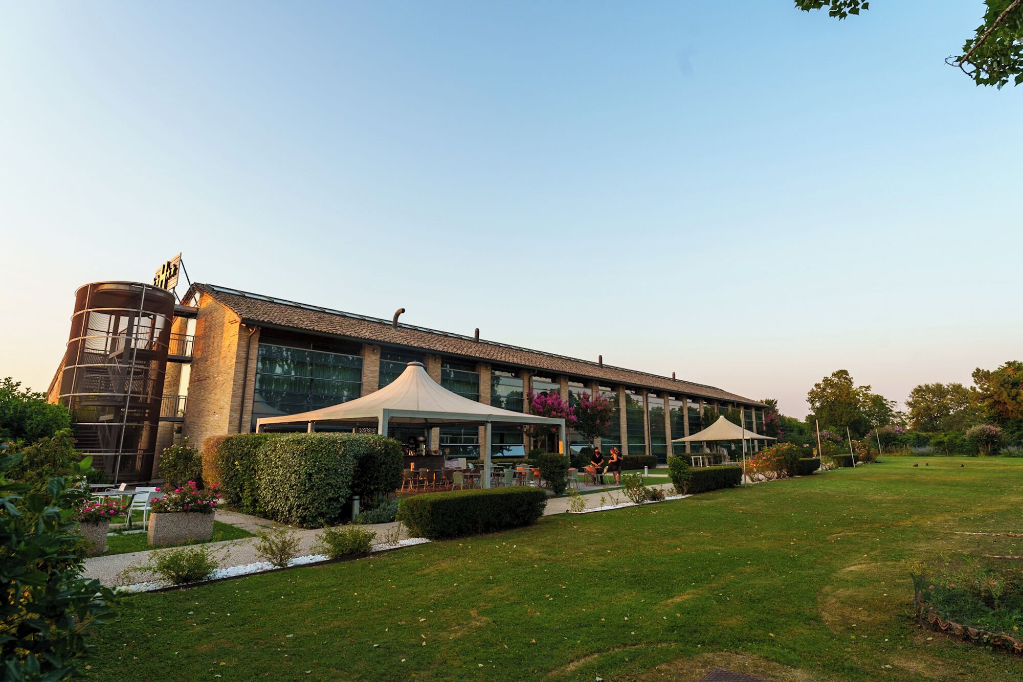 A modern building with a cylindrical structure, outdoor seating, and a well-maintained garden.
