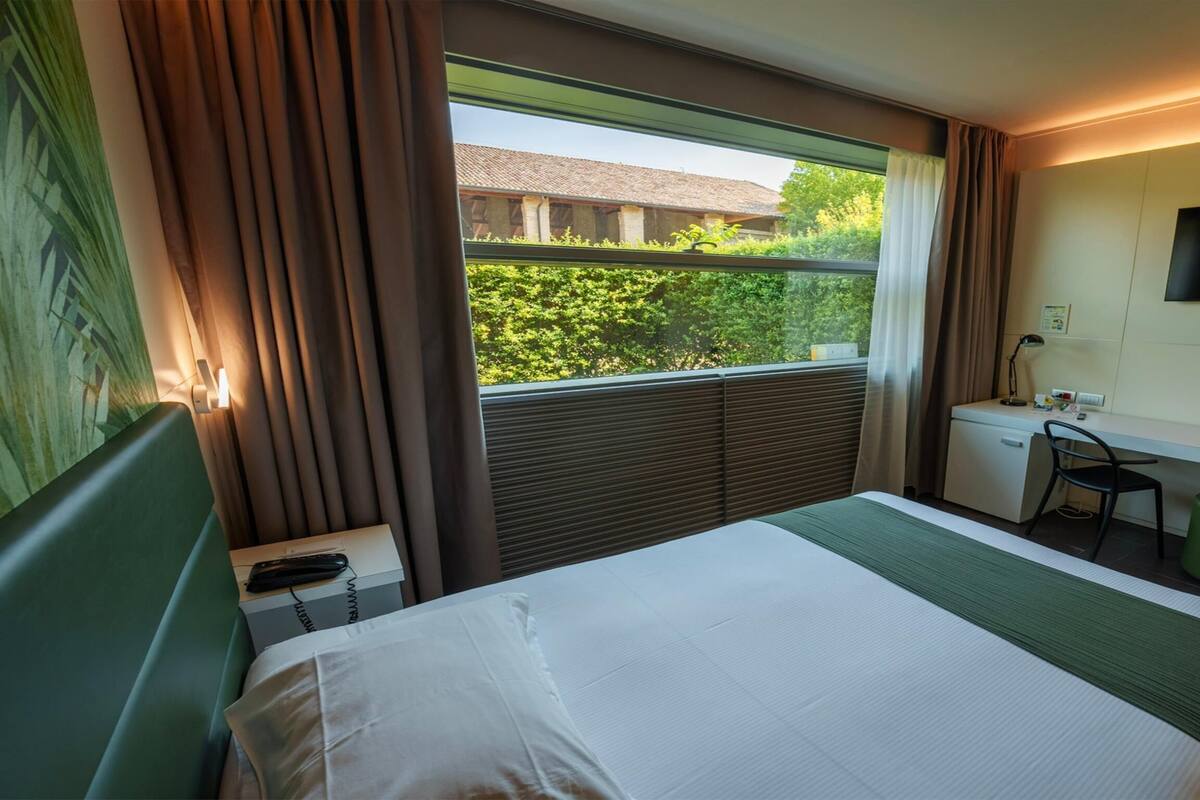 A hotel room with a bed, a desk, a chair, a TV, and a window with curtains.