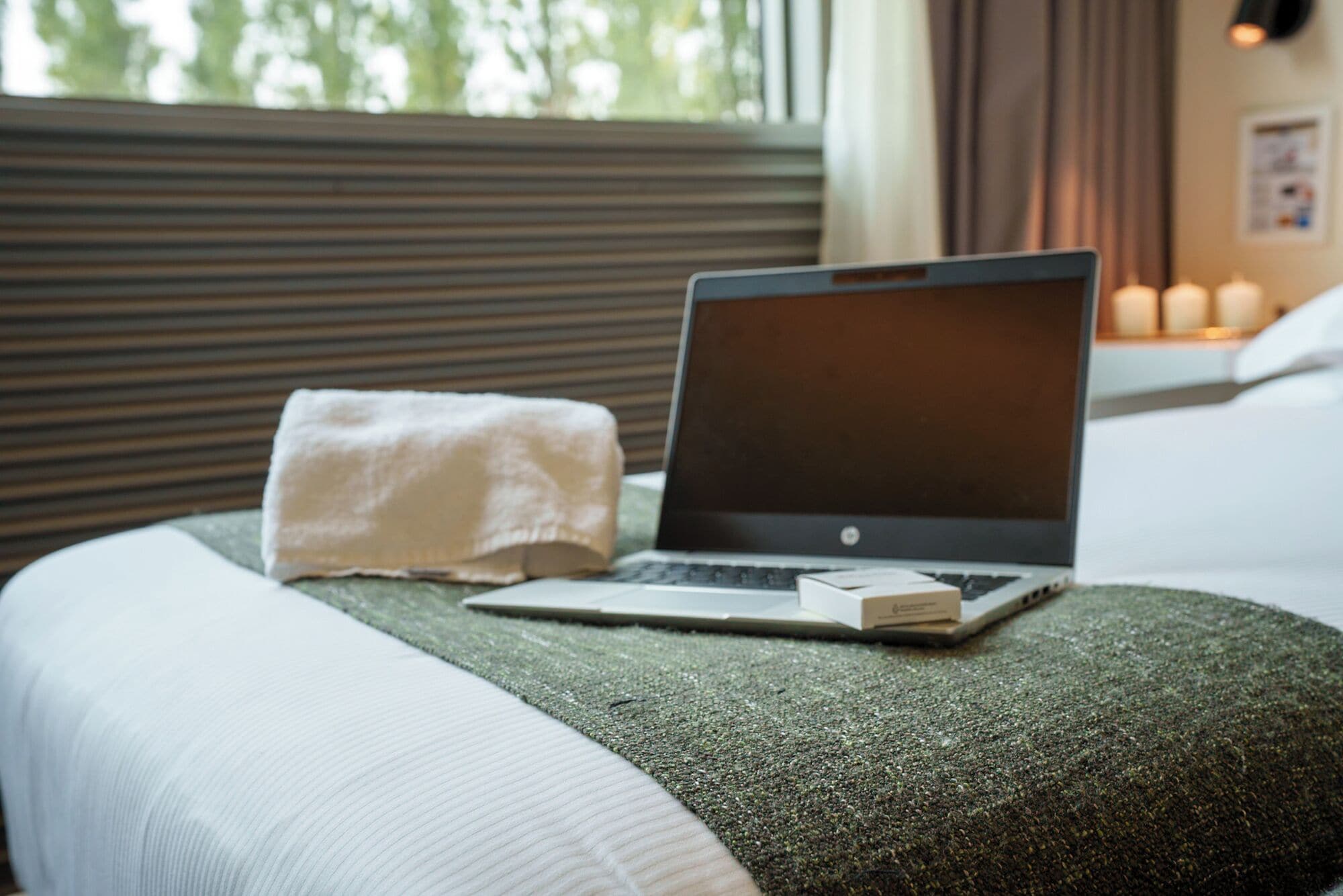 A laptop on a bed with a white pillow and a green blanket.