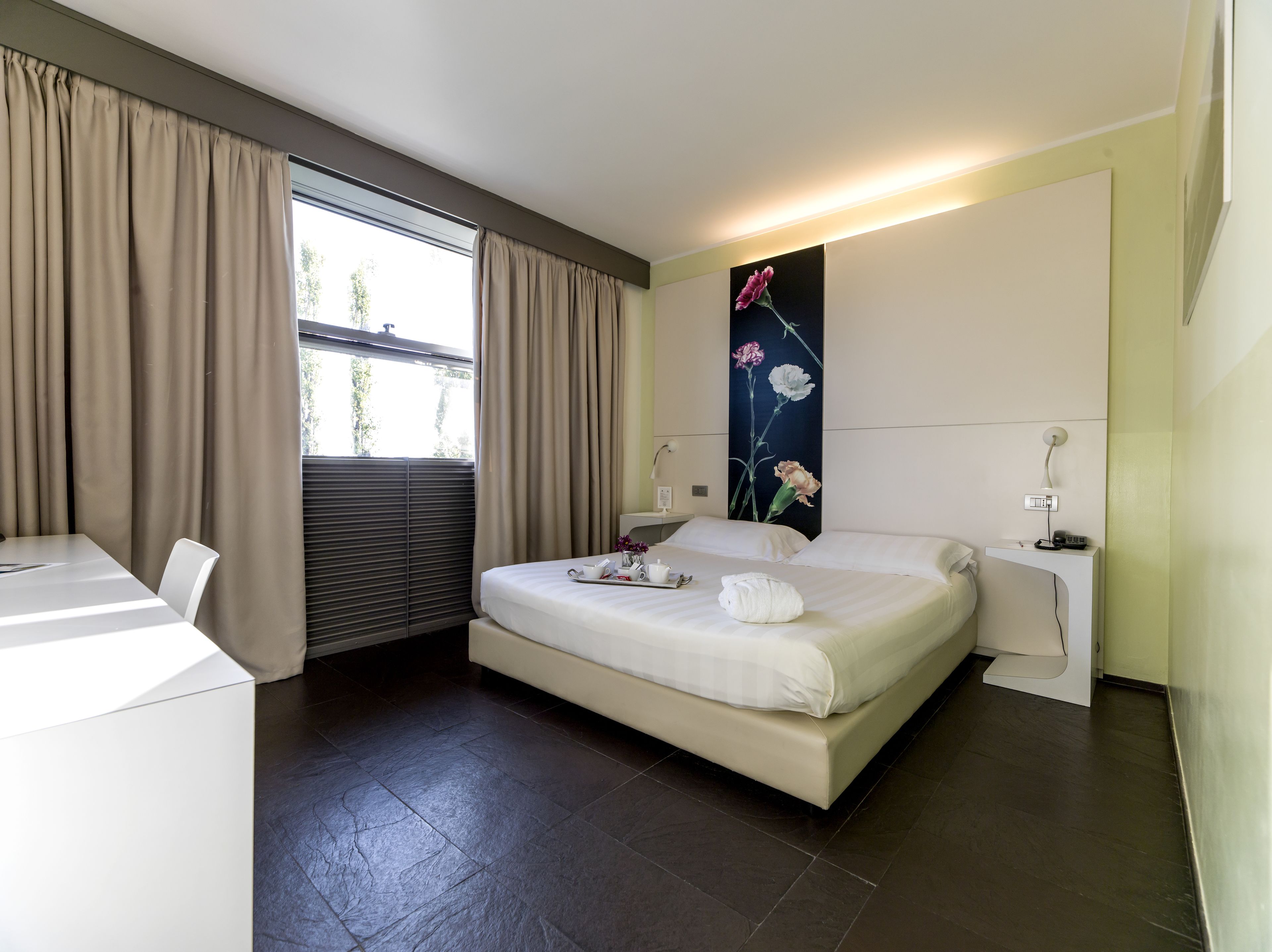 A modern hotel room with a bed, a desk, and a large window with curtains.