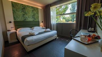 Une chambre d’hôtel avec un lit, une table de chevet, un bureau et une vue sur les arbres par la fenêtre.