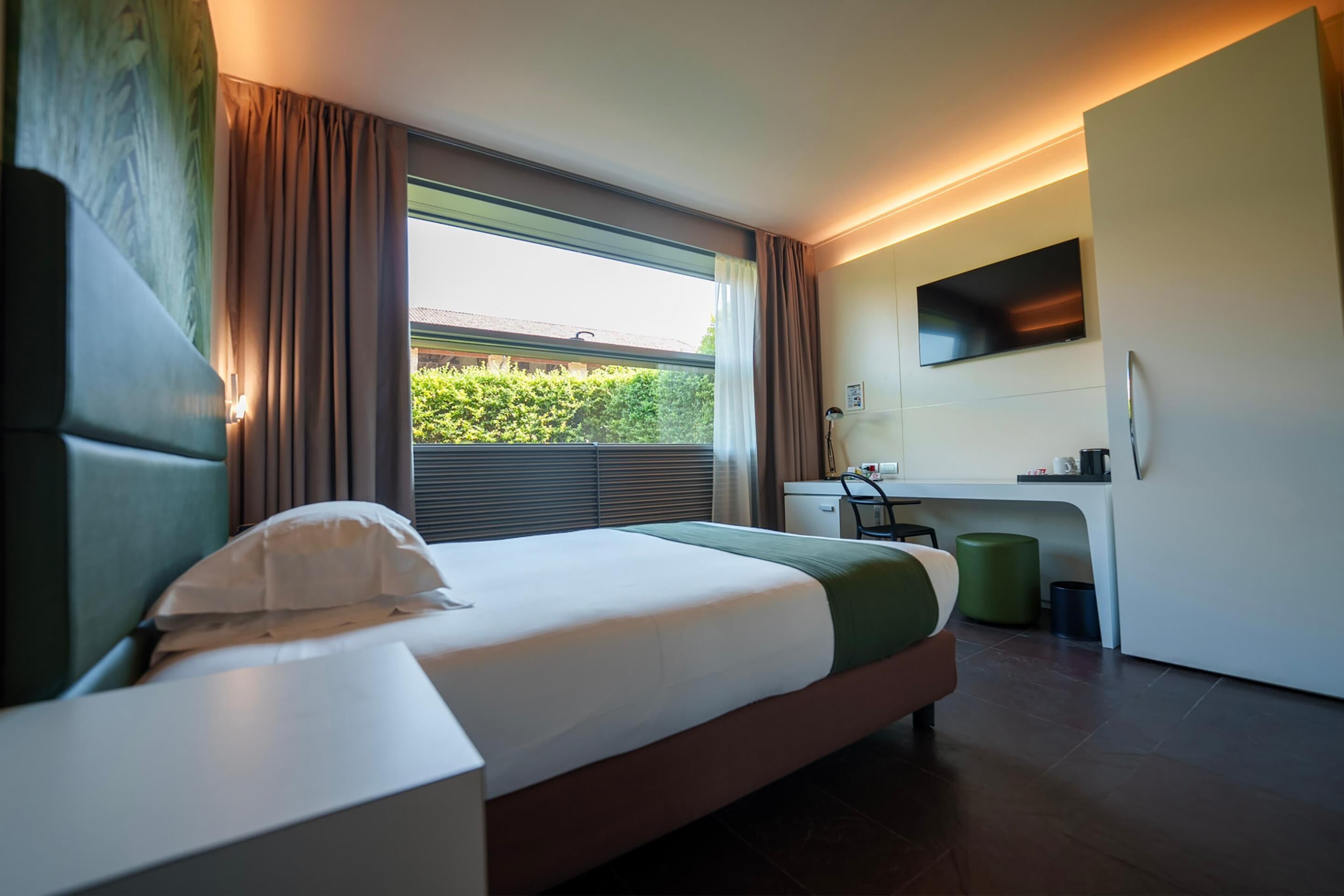 Una camera d'albergo moderna con un letto, una scrivania, una televisione e una finestra con tende.