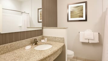 Une salle de bain avec un lavabo doté d’un plan de travail en granit, un miroir, une œuvre d’art encadrée, un porte-serviettes et des toilettes.