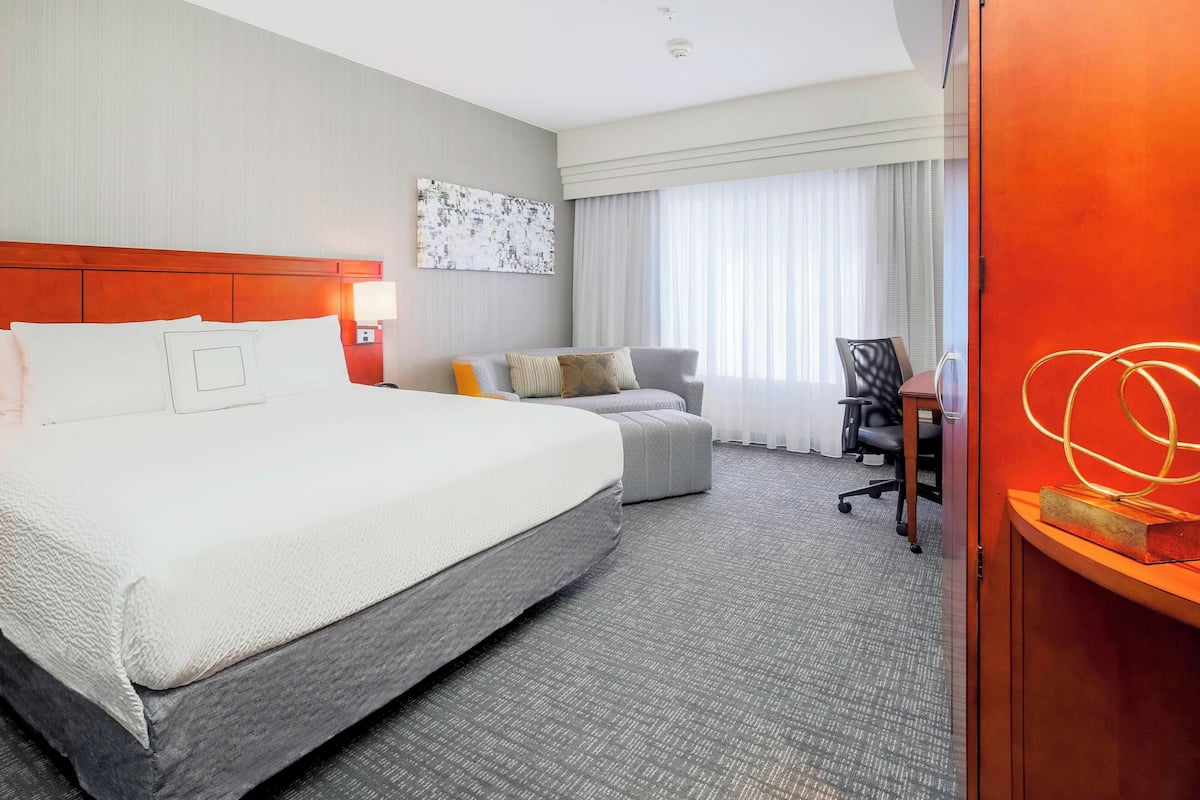 A hotel room with a large bed, a sofa, a desk, and a chair.