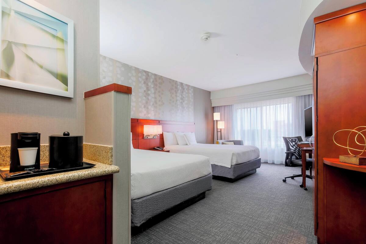 A hotel room with two beds, a desk, a chair, a coffee maker, and a TV.