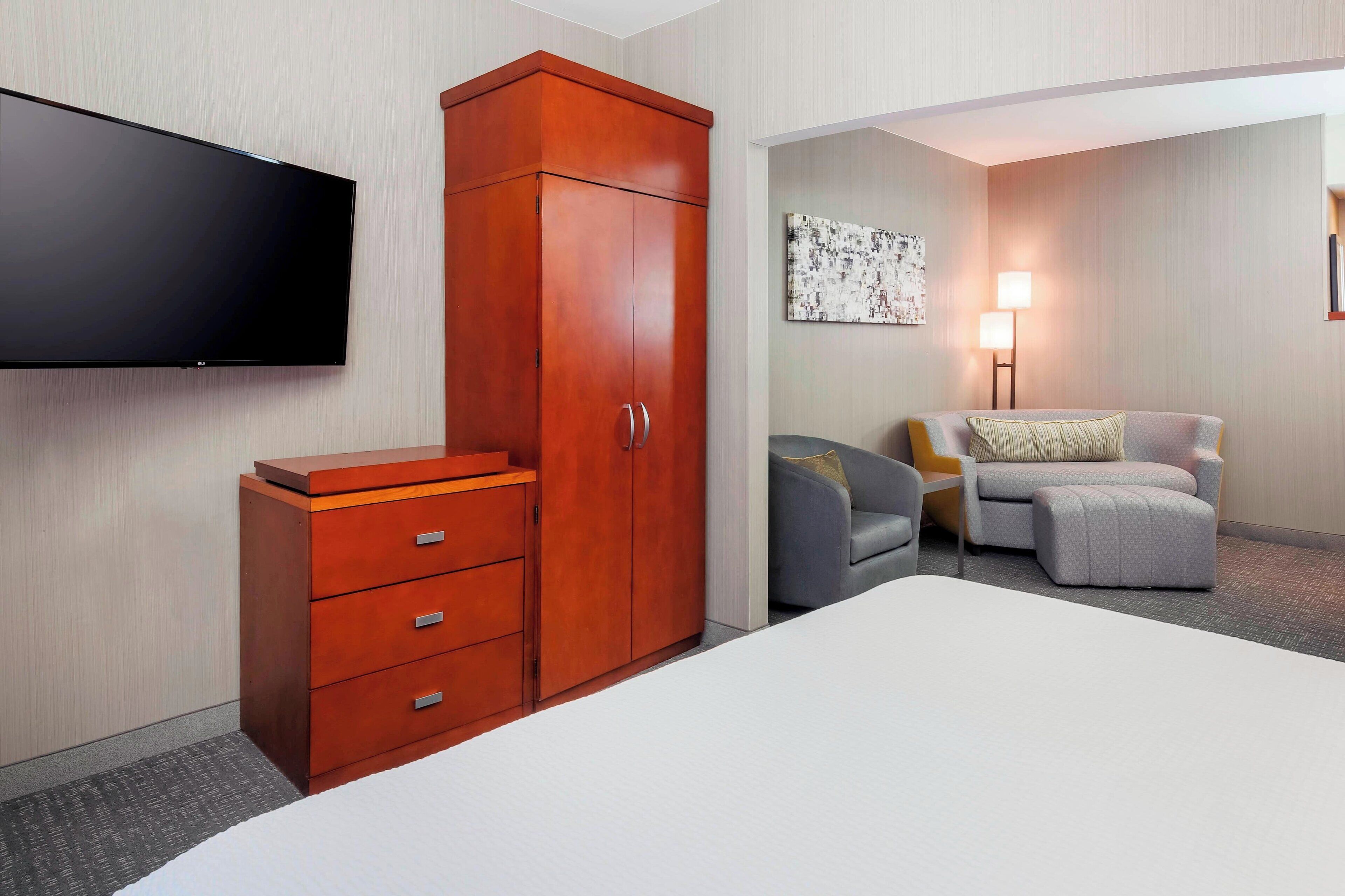 Quarto de hotel com cama grande, guarda-roupa, televisão de ecrã plano, sofá e uma lâmpada.