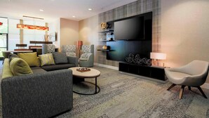 Ein modernes Wohnzimmer mit einer Couch, Sesseln, einem Couchtisch und einem an der Wand befestigten Fernseher.