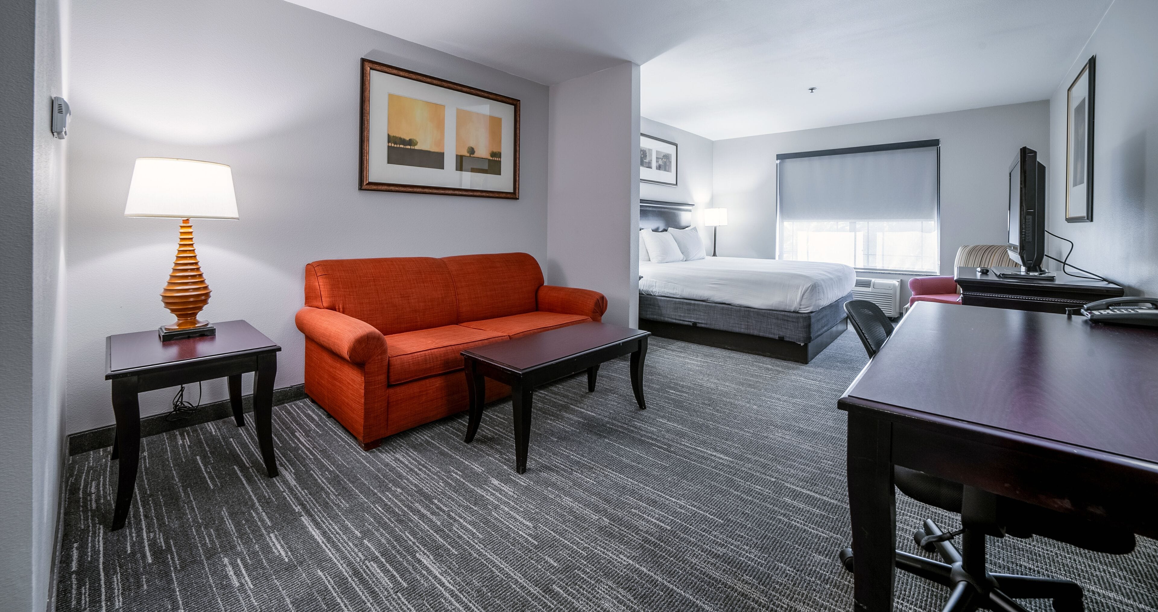 A hotel room with a bed, a sofa, a desk, and a lamp.