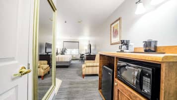 A hotel room with a kitchenette, a large mirror, a sofa, a television, and a bed.