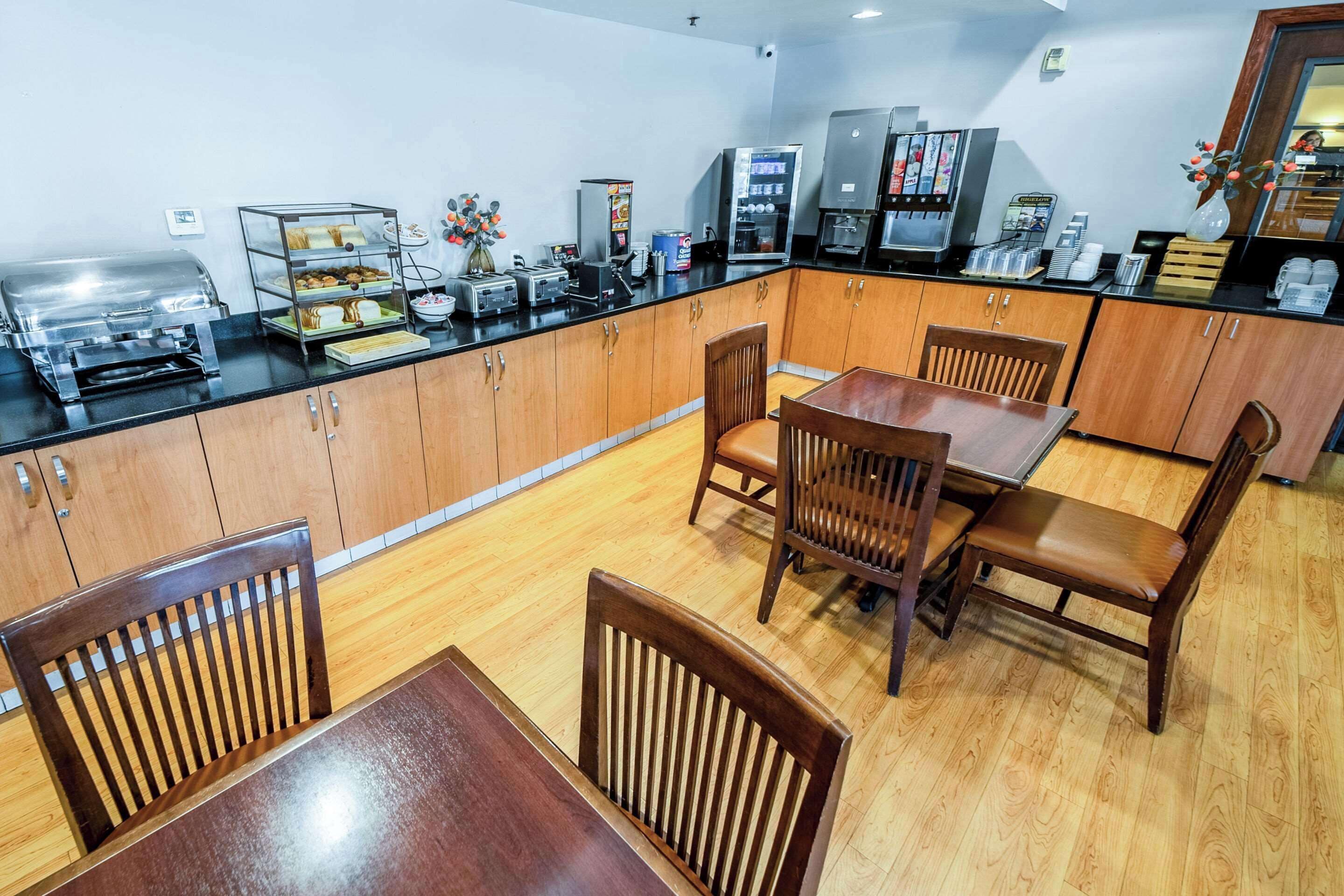Un área de desayuno con mesas de buffet, máquinas de café y disposición de mesas.