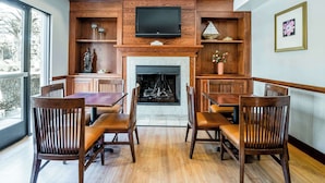 A dining area with a fireplace, wooden furniture, and a television mounted above. - Country Inn & Suites by Radisson, Ontario at Ontario Mills, CA (Ontario)