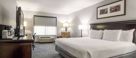 Habitación de hotel con cama, escritorio, lámparas y un ventanal grande.