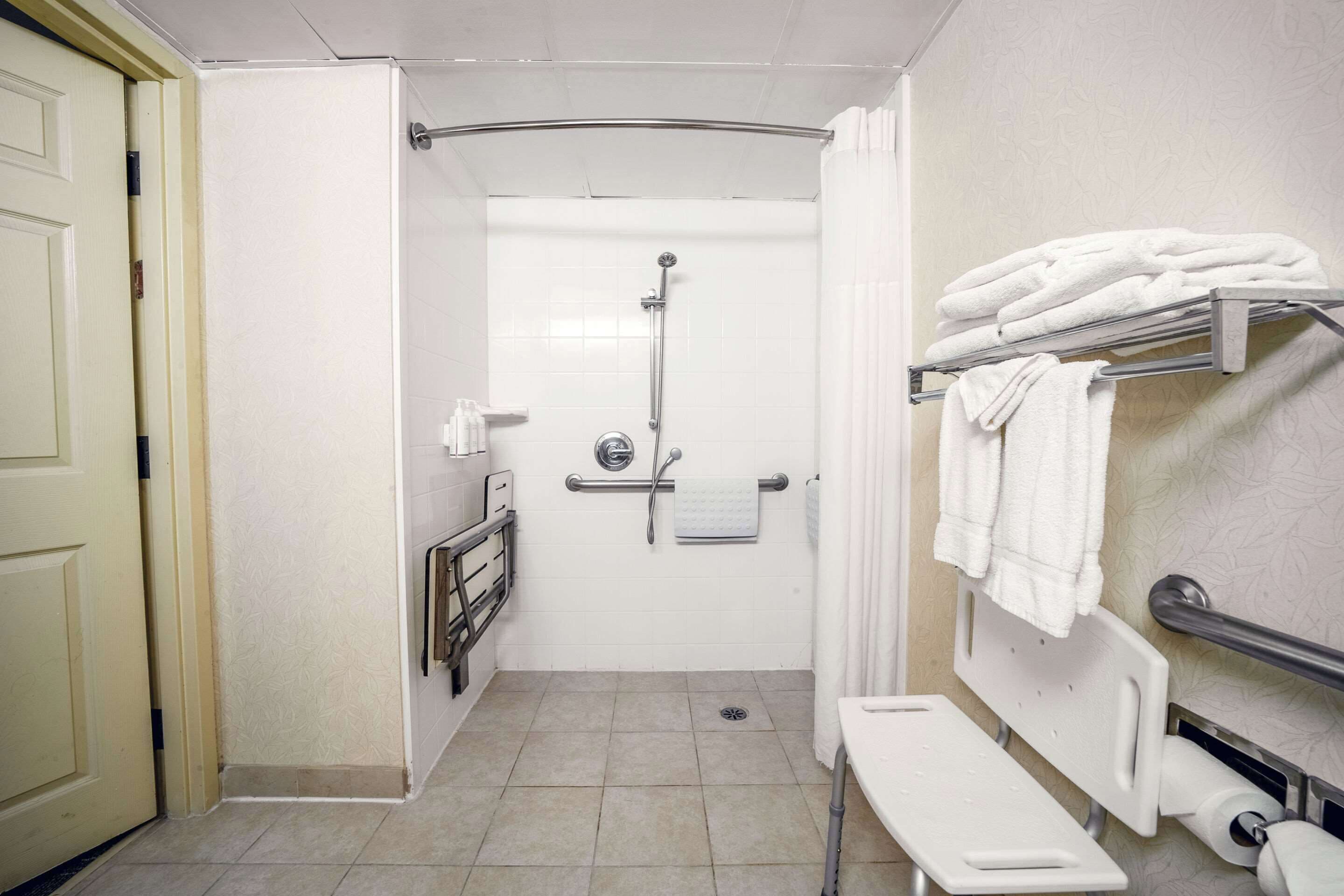 A bathroom with a shower, a bench, a towel rack, and a toilet paper holder.
