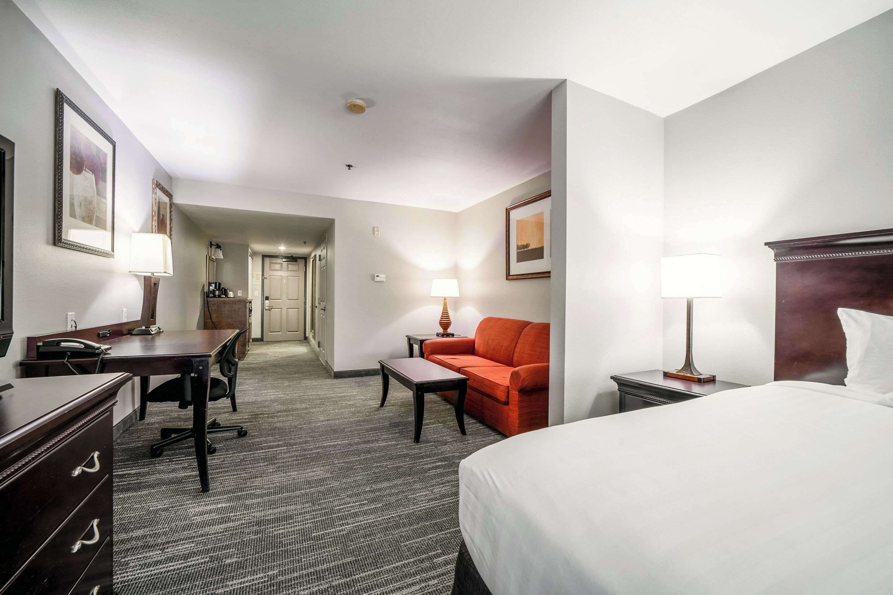 A hotel room with a bed, desk, chair, and a sofa.
