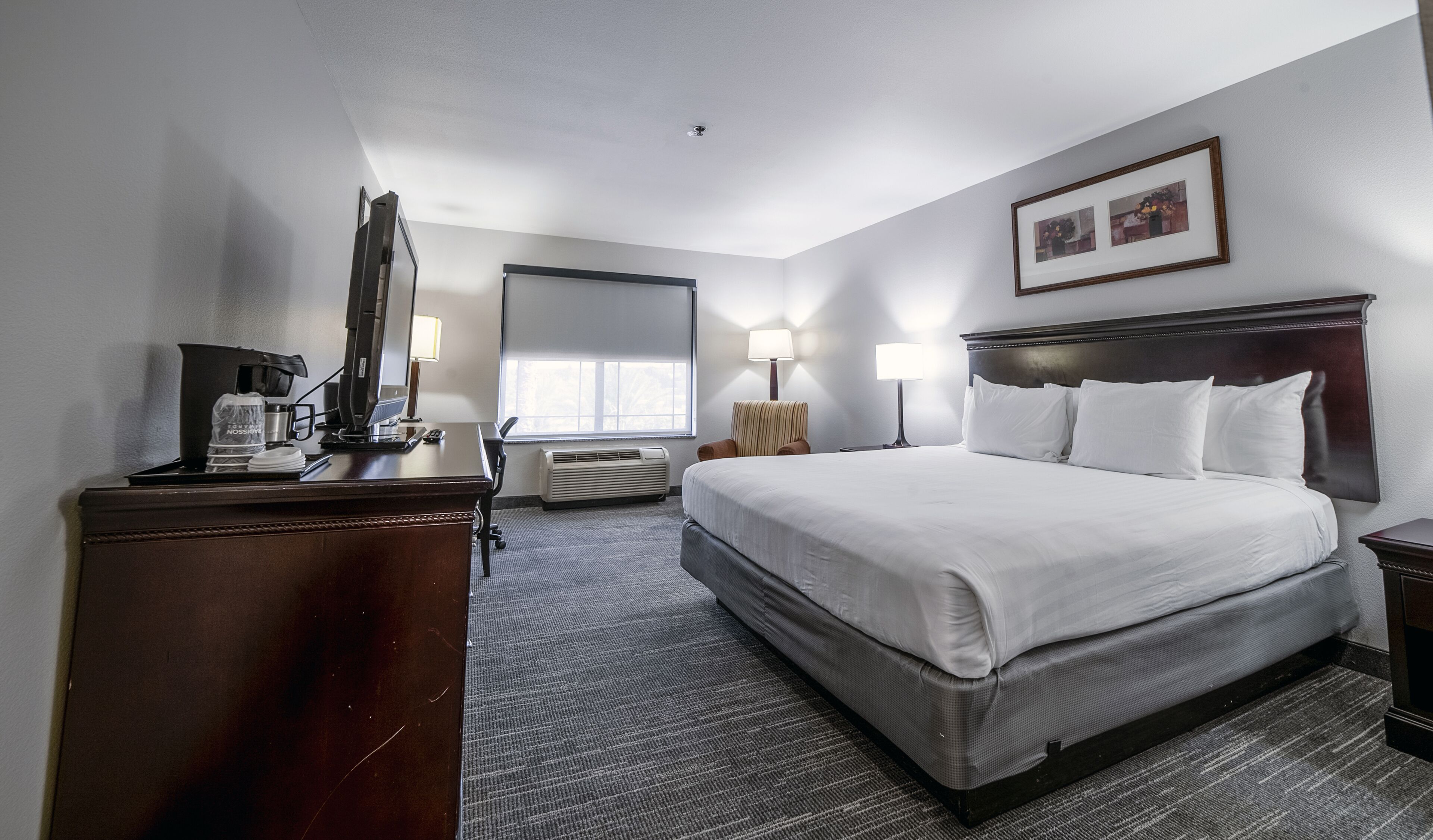 A hotel room with a large bed, a desk with a computer, a chair, a lamp, and a picture on the wall.