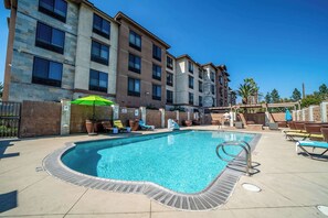 A swimming pool with lounge chairs and umbrellas, surrounded by a multi-story building with a stone facade. - Country Inn & Suites by Radisson, Ontario at Ontario Mills, CA (Ontario)