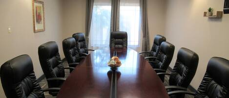 Un salón de conferencias con una larga mesa, sillas de cuero negro, un florero con flores y un cuadro en la pared.