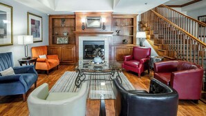 A spacious living room with a fireplace, leather sofas, a glass coffee table, and a wooden staircase. - Country Inn & Suites by Radisson, Ontario at Ontario Mills, CA (Ontario)