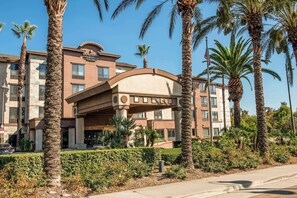 A hotel with a prominent entrance, palm trees, and a clear blue sky. - Country Inn & Suites by Radisson, Ontario at Ontario Mills, CA (Ontario)