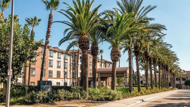 A hotel with a row of palm trees, a parking lot, and a sign that reads 'Country Inn & Suites.' - Country Inn & Suites by Radisson, Ontario at Ontario Mills, CA (Ontario)